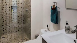 A bathroom with a shower area tiled with small square tiles, a white sink, a mirror, and two bottles of hand soap. - Acogedor Departamento a 7 minutos de Coyoacán + Bonita azotea. (Ciudad de México)