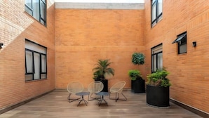 A courtyard with brick walls, wooden flooring, and three chairs. There are potted plants and a small tree. - Acogedor Departamento a 7 minutos de Coyoacán + Bonita azotea. (Ciudad de México)