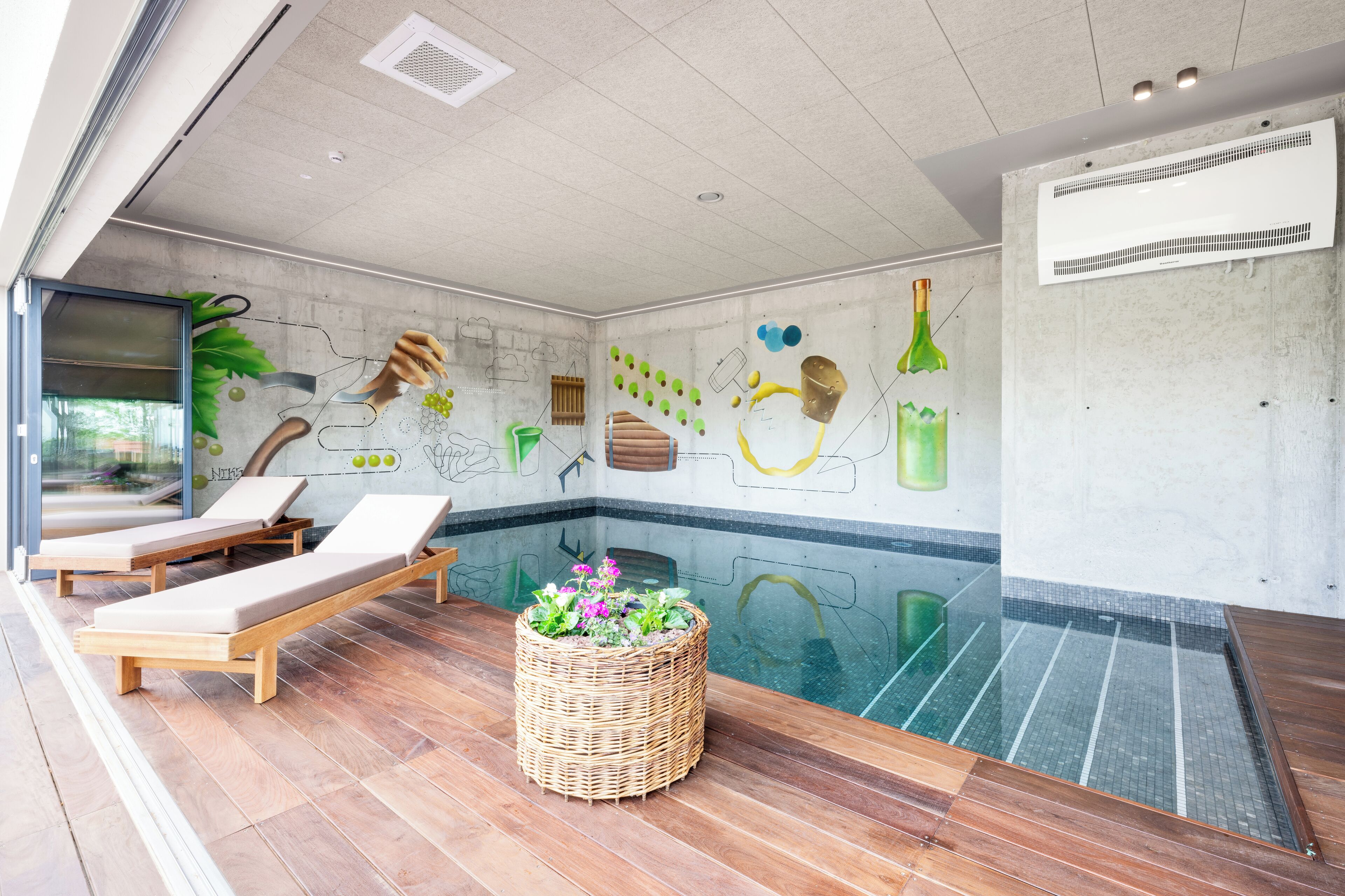 A modern indoor pool area with lounge chairs, a decorative wall mural, and a clear glass pool.