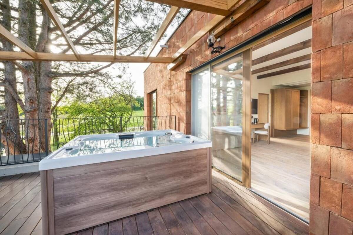 A modern outdoor hot tub area with a wooden deck, a glass enclosure, and a view of the surrounding landscape.