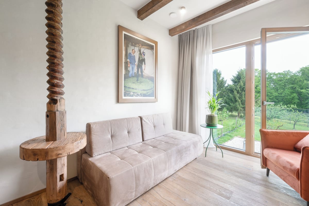A modern living room with a beige sofa, a wooden table, and a large window with a view of greenery.