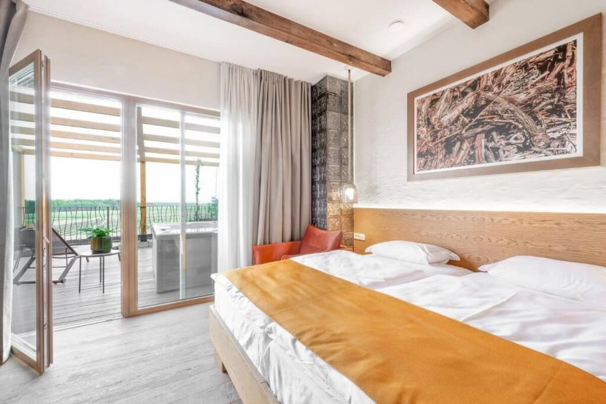 A hotel room with a bed, a balcony with a table and chairs, and a large painting on the wall.