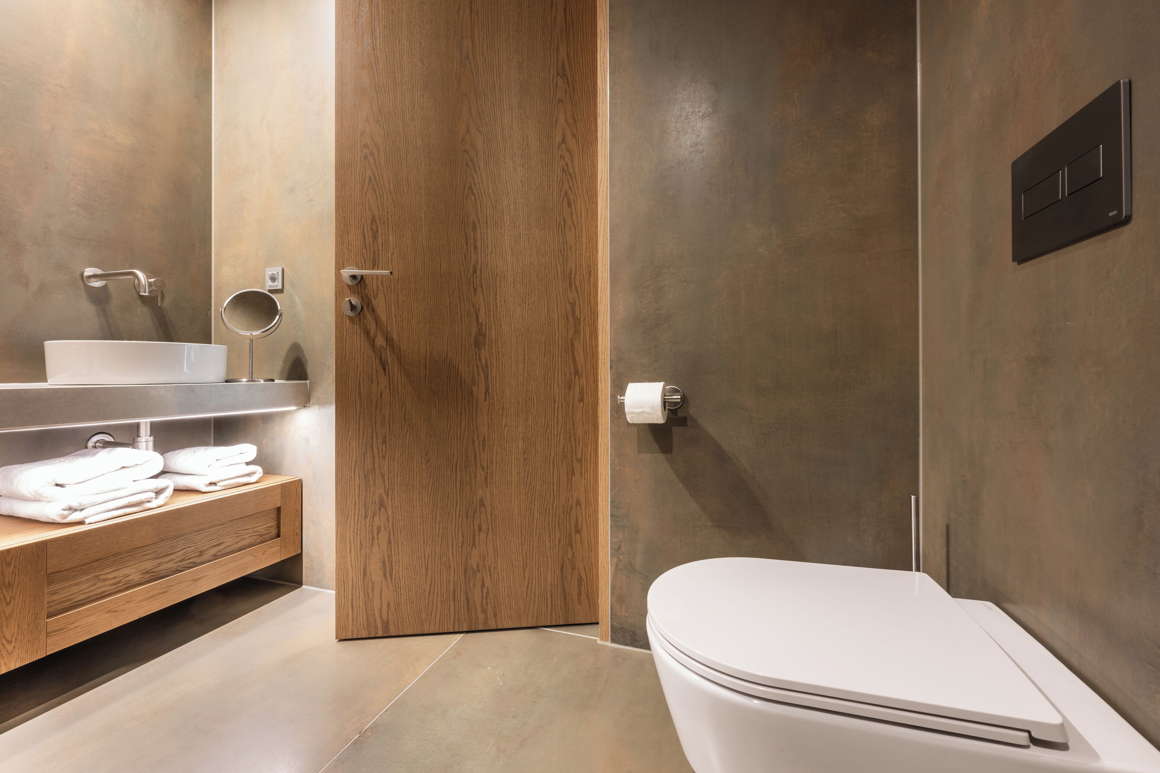A modern bathroom with a wooden vanity, a white sink, and a toilet.