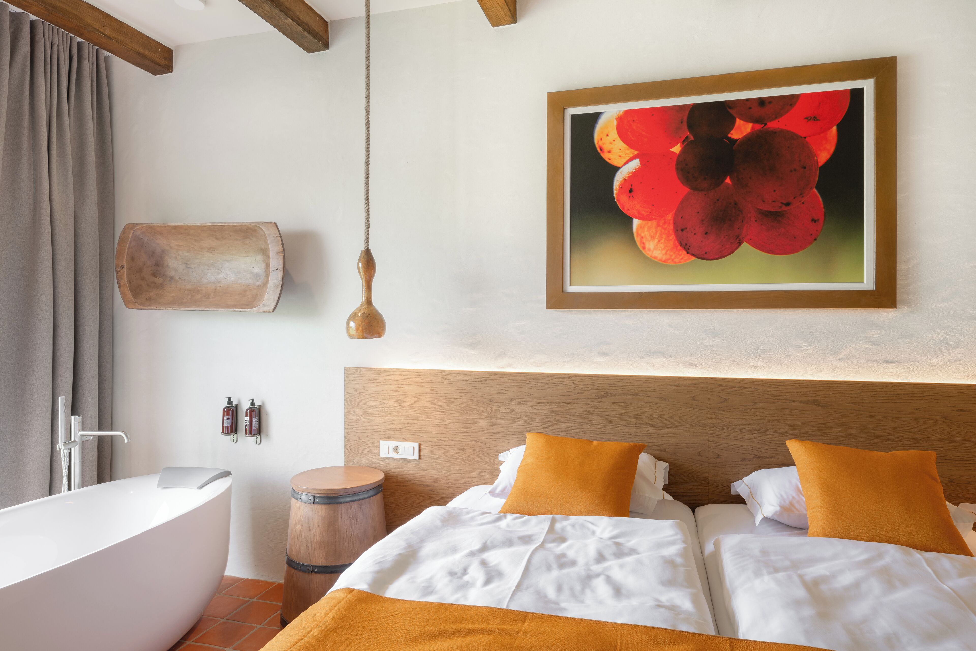 A modern bedroom with a large bed, a wooden headboard, a painting of red flowers, a bathtub, and a wooden barrel.