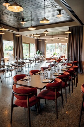 A restaurant with tables set for dining, red upholstered chairs, and hanging pendant lights. - Hisa Marija House (Ormoz)