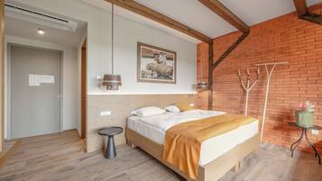 A bedroom with a wooden bed, a small round table, a wall-mounted light, and a brick wall.