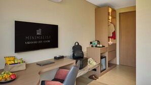 A modern hotel room with a flat-screen TV, a desk with a laptop, a chair, a small fridge, a wooden wardrobe, and a shoe rack. - Minimaist - Varanasi City Centre (Varanasi)