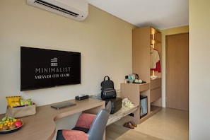 Habitación de hotel moderna con televisión de pantalla plana, escritorio con computadora portátil, silla, refrigerador pequeño, armario de madera y zapatero.