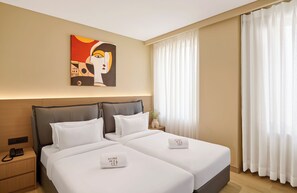 Habitación de hotel con dos camas, un cuadro en la pared, una mesita de noche con un teléfono y una ventana con cortinas.