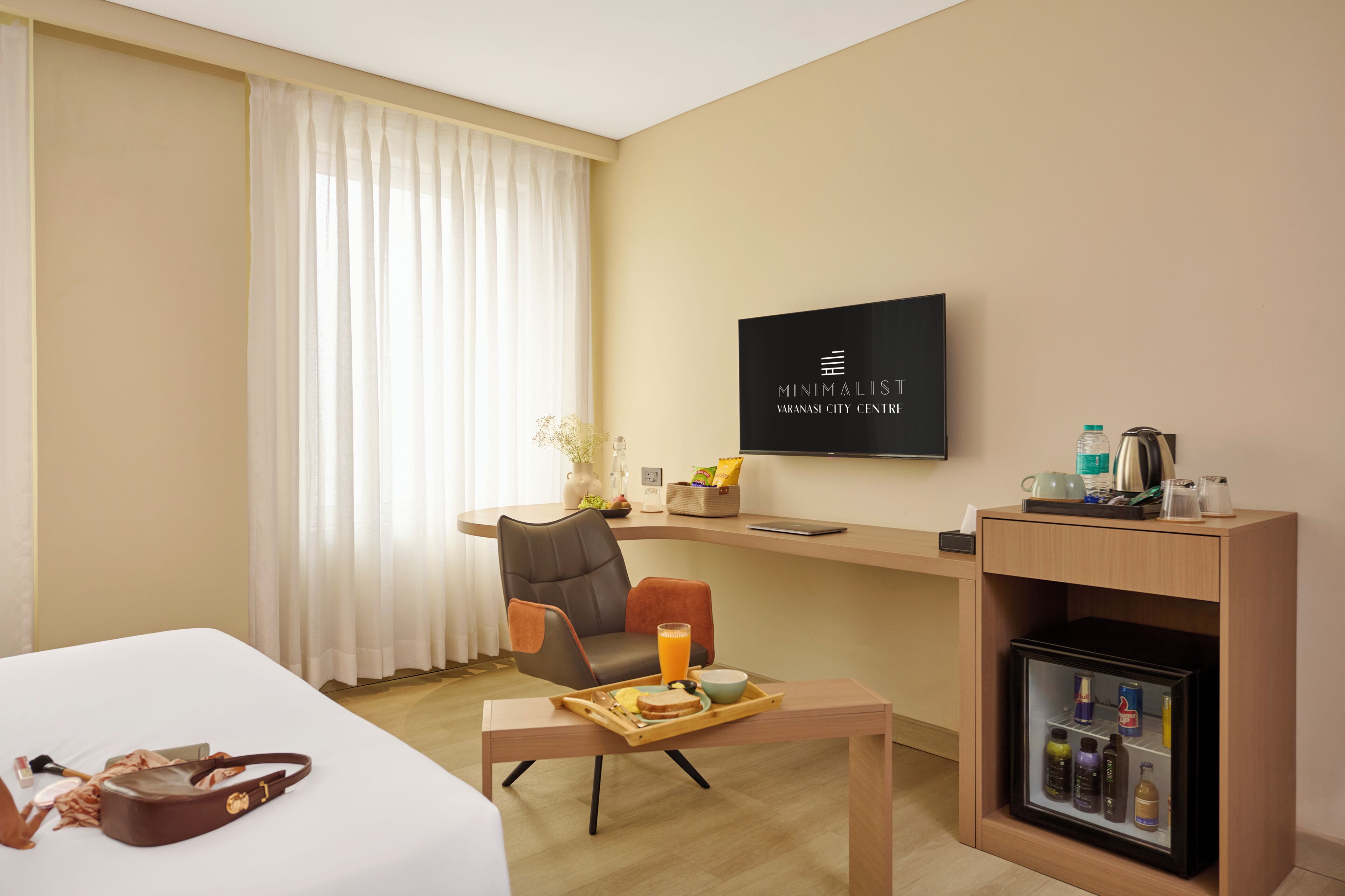 Habitación de hotel con cama, escritorio con silla, televisión, minibar y ventana con cortinas.
