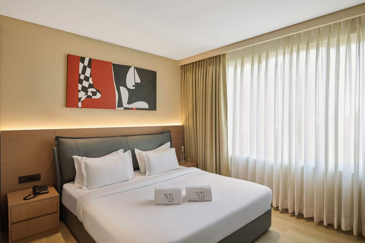 Habitación de hotel con una cama grande, una mesita de noche, teléfono en la pared y una ventana con cortinas.