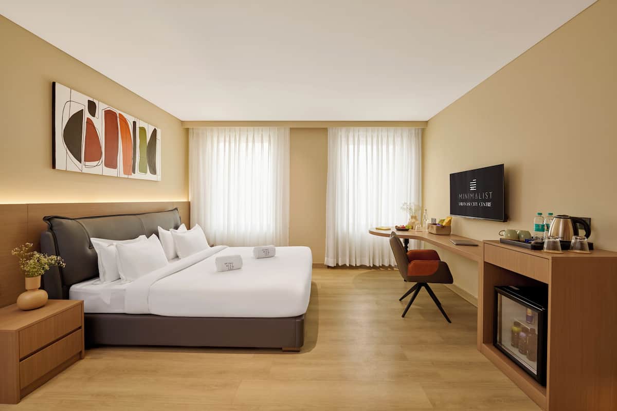 Moderni hotellihuone, jossa on sänky, yöpöytä, työpöytä, tuoli, televisio ja minibaari.