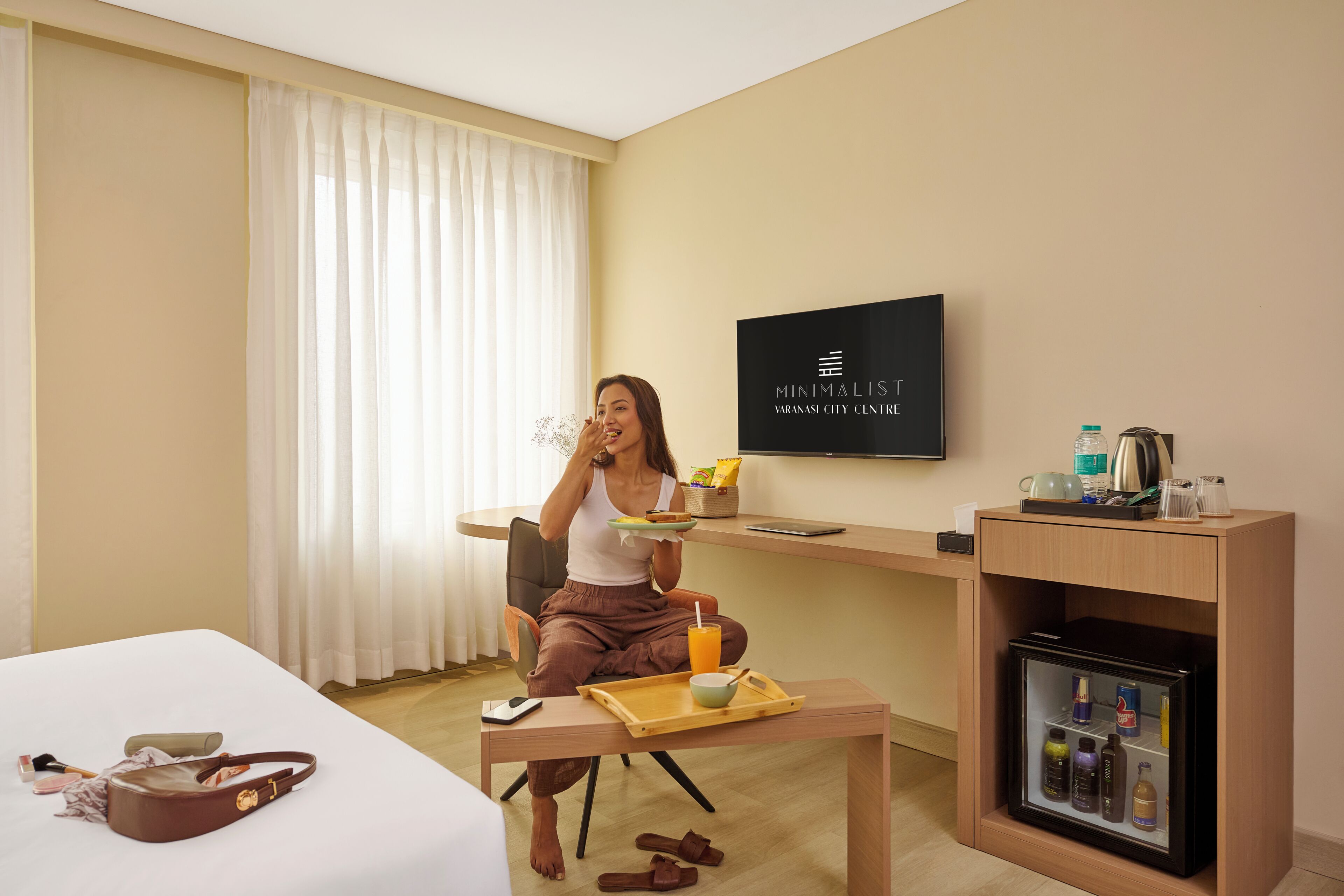Habitación de hotel con cama, escritorio con televisor, minibar y zona de comedor con bandeja.