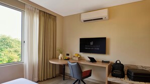 A hotel room with a bed, a desk with a laptop, a chair, a TV on the wall, and a suitcase on a bench. - Minimaist - Varanasi City Centre (Varanasi)