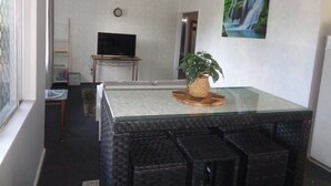 Uma sala de estar com uma mesa de centro de vidro, uma televisão em um suporte, um relógio na parede e um quadro de uma cachoeira.