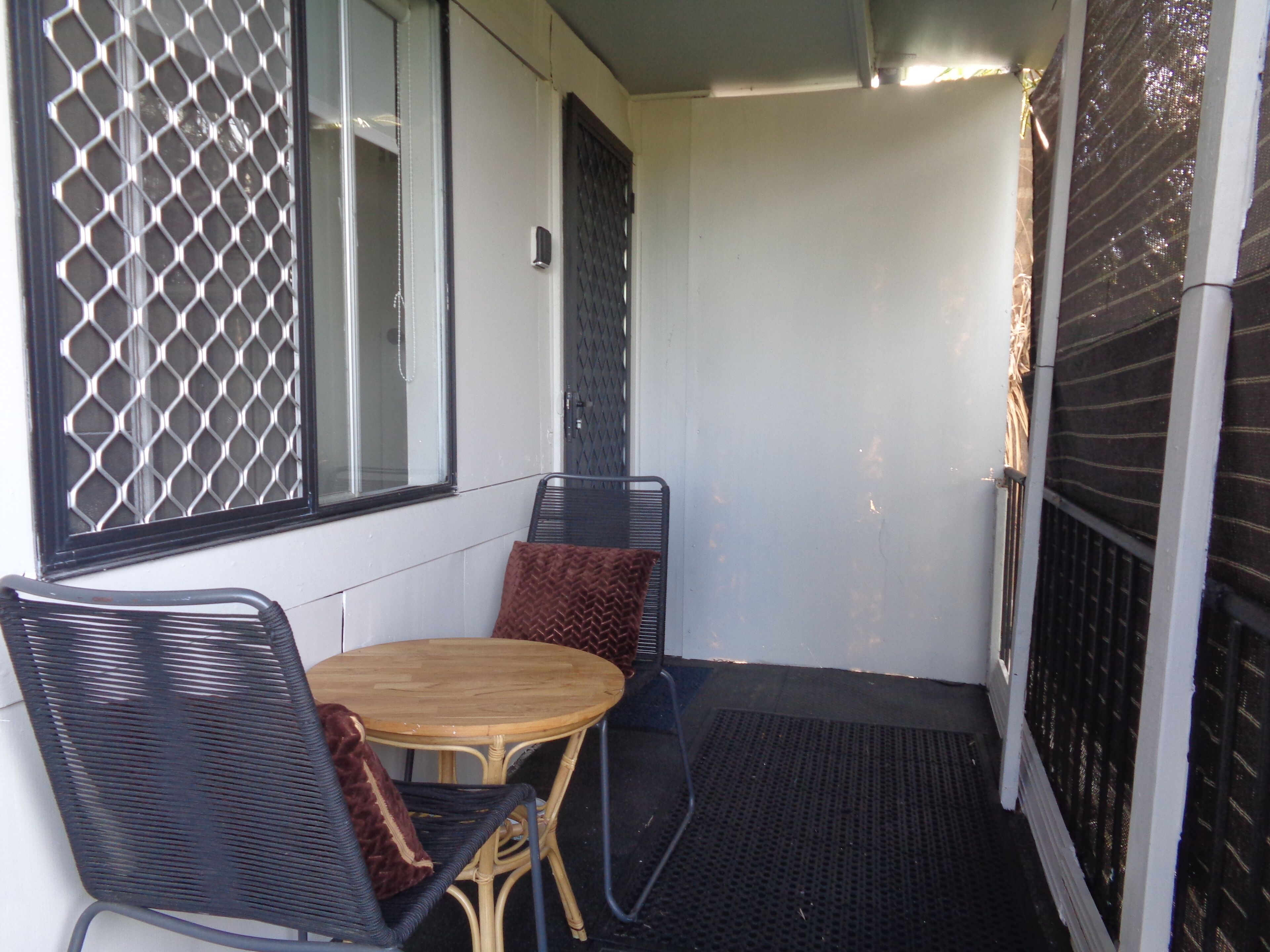 Un petit espace extérieur aménagé avec une table ronde et deux chaises, une fenêtre dotée d’un grillage métallique et une porte avec une grille métallique.