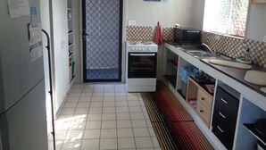 Cozinha com geladeira branca, fogão e pia. Há uma janela com vista para o verde lá fora.