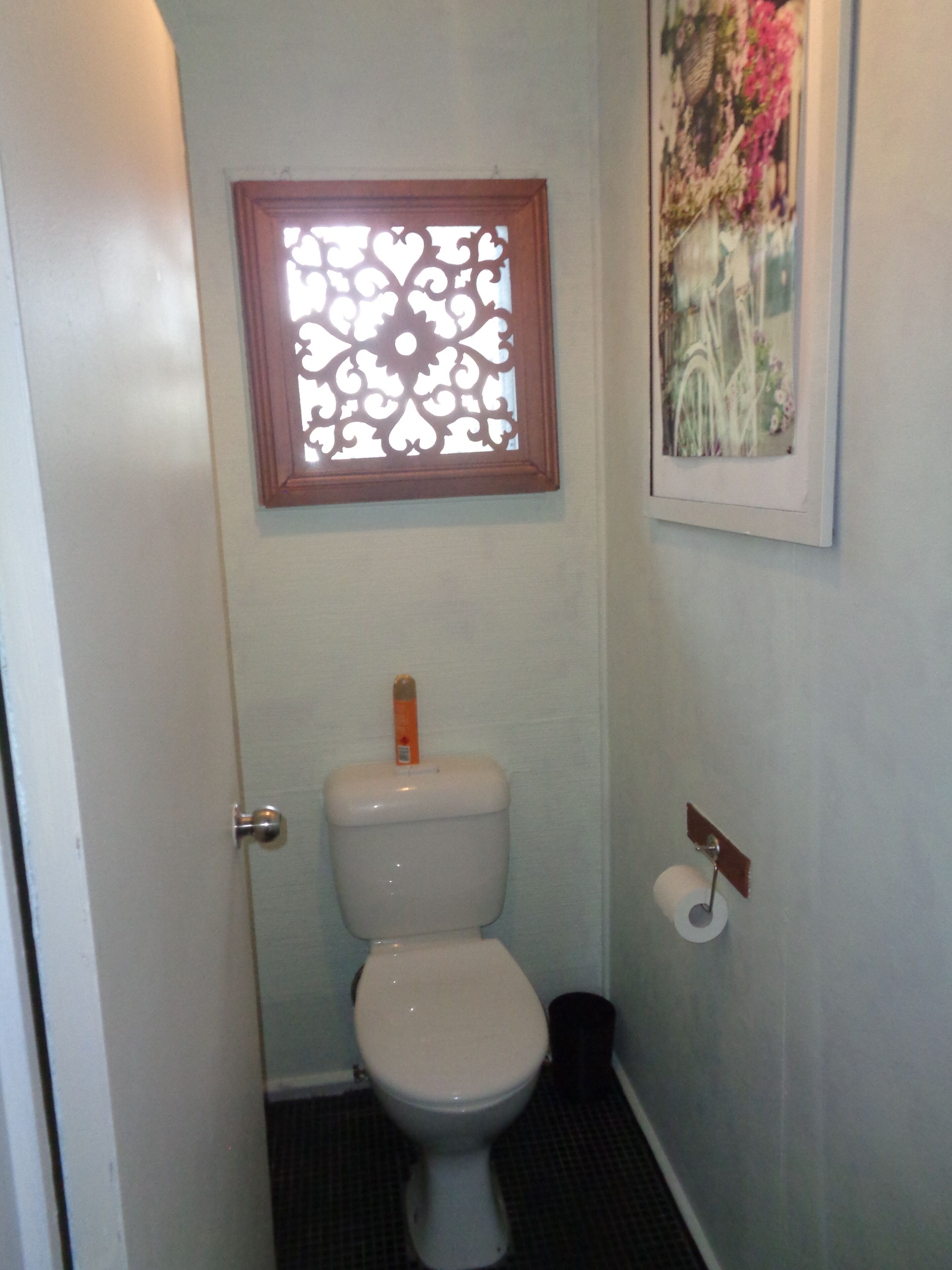 Een kleine badkamer met een toilet, een raam met decoratieve lijst en een toiletrolhouder.