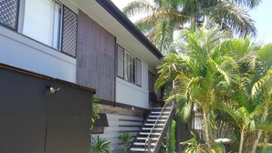 Um edifício moderno com uma escadaria que leva a uma varanda, rodeado por plantas tropicais exuberantes.