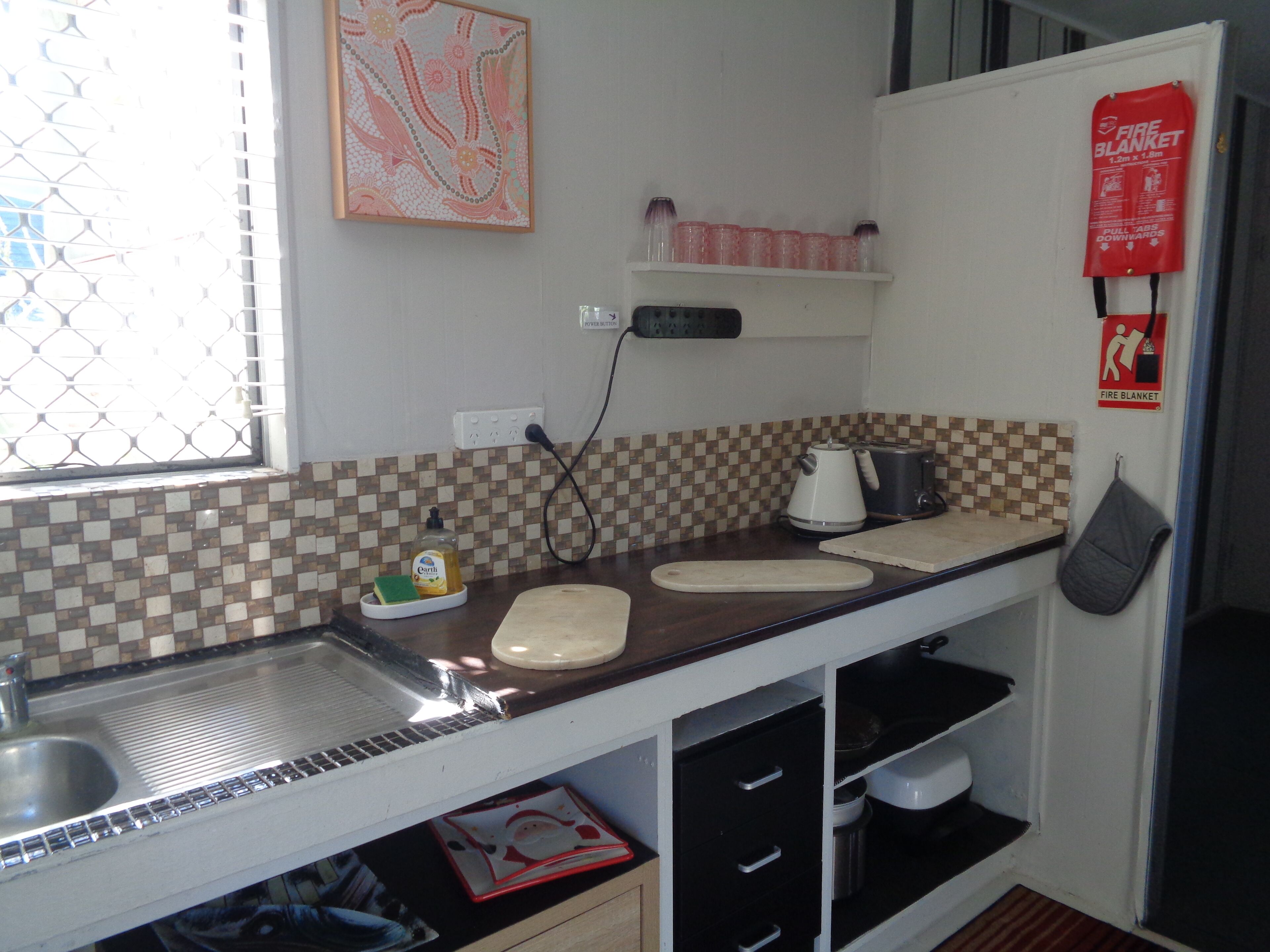 A compact kitchen with a sink, countertop, and a fire blanket mounted on the wall.