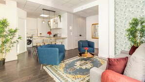 A modern living room with a blue sofa, a patterned rug, and a kitchen in the background. - Merveil Family Suite - Sebastopol III (Paris)