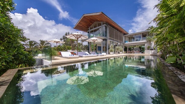 Un resort moderno con piscina cristalina, zona de descanso y exuberante vegetación tropical.