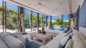 Un salón moderno con un sofá grande, una mesa de centro y vistas a un jardín tropical a través de amplios ventanales.