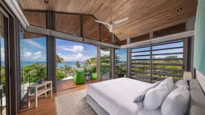 Un dormitorio moderno con una cama grande, vistas al océano y un balcón con plantas.