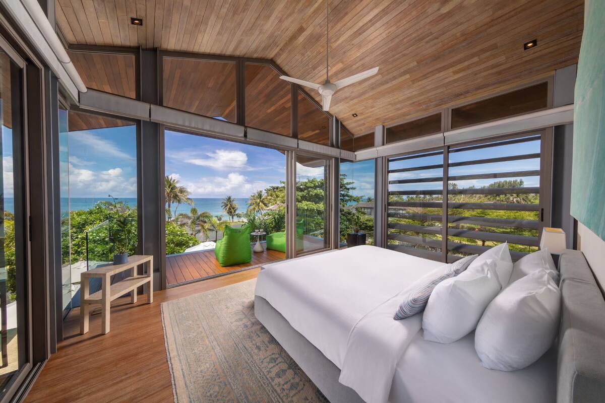 A modern bedroom with a large bed, a view of the ocean, and a balcony with plants.