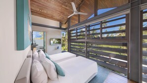 Un dormitorio moderno con una cama grande, un ventilador de techo y vistas a palmeras a través de una puerta corredera.