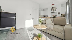 A modern living room with a sofa, a small round table, and a potted plant. - Exclusive 2 Bedroom Flat near Loughborough Junction! (Greater London)