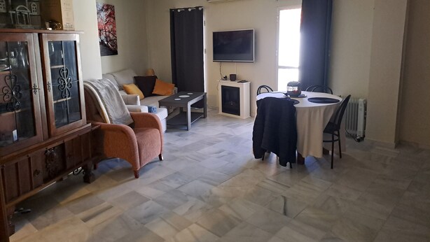 A living room with a sofa, a dining table with chairs, a TV mounted on the wall, and a cabinet with decorative items. - Charming apartment for couples - discover magical Seville! (Tomares)
