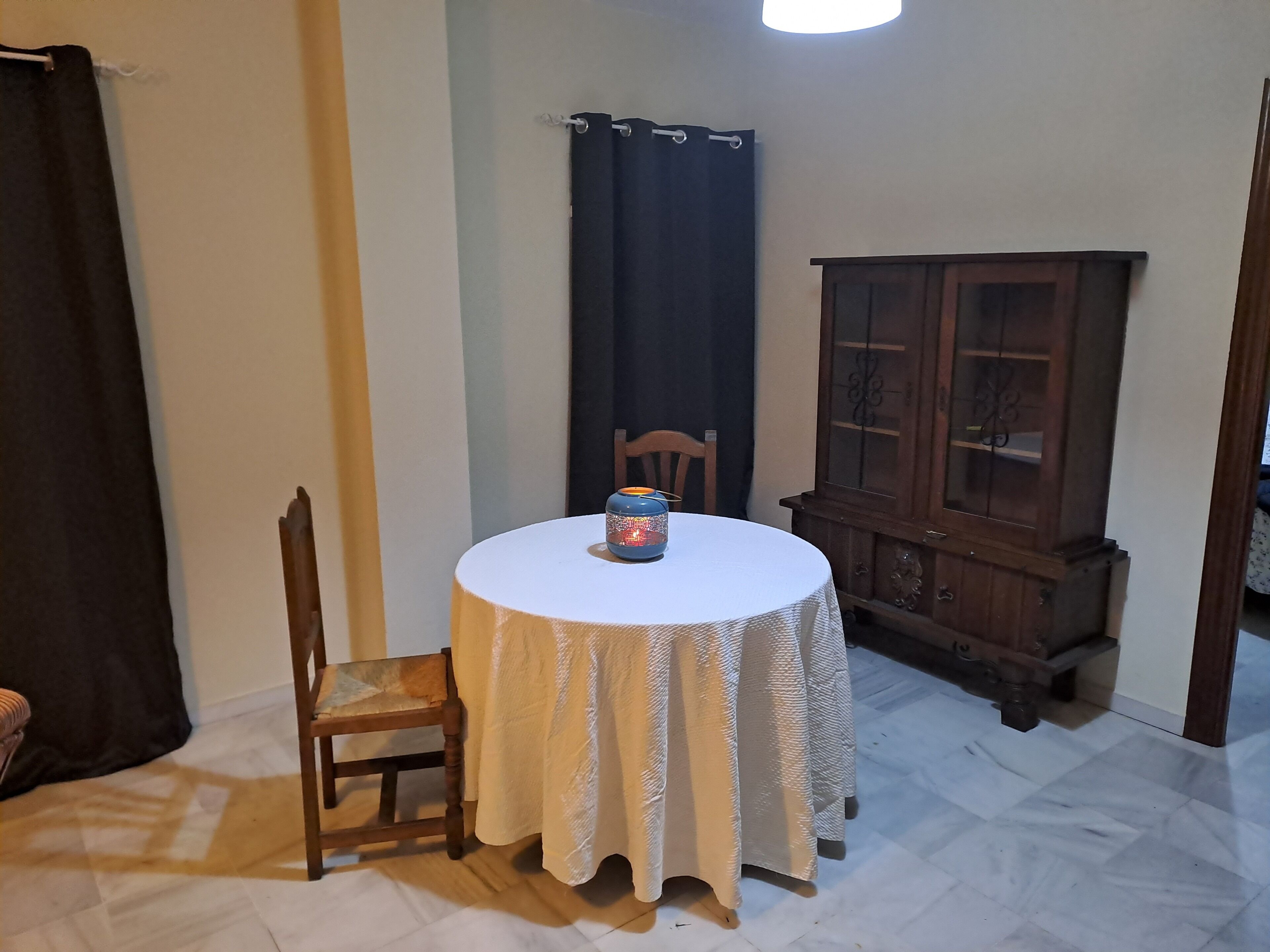 A small dining area with a round table, a chair, a cabinet, and a curtain.