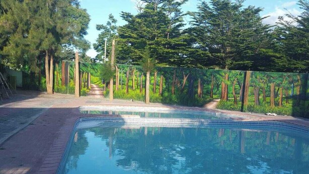 A rectangular swimming pool with a tiled edge, surrounded by a brick walkway and a wooden fence. - Royal Shalom Lodge (Lusaka)