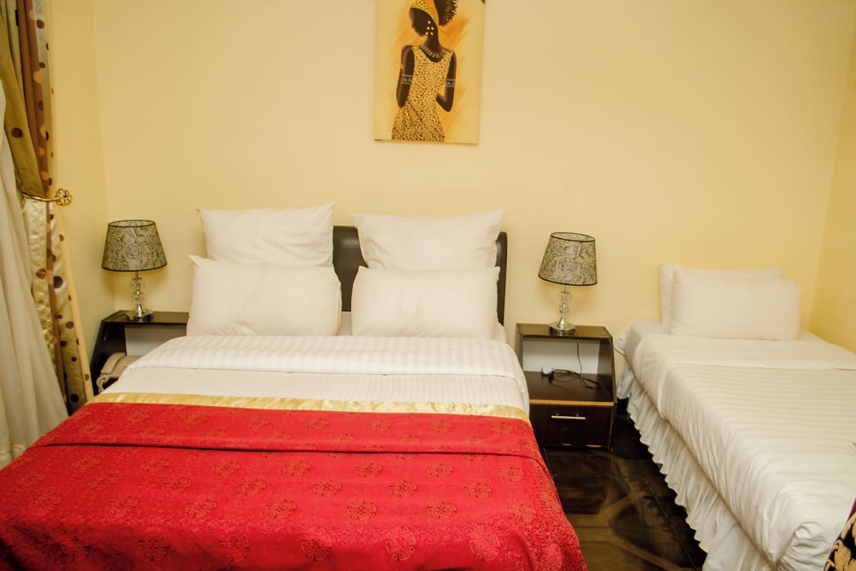 Een hotelkamer met een groot bed, twee nachtkastjes, een rode spreidekker en een schilderij aan de muur.