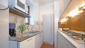 Una cocina compacta con armarios blancos, microondas, cafetera y estufa a gas.