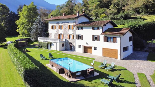 Una casa de dos pisos con piscina, mobiliario exterior y una escalera de piedra.