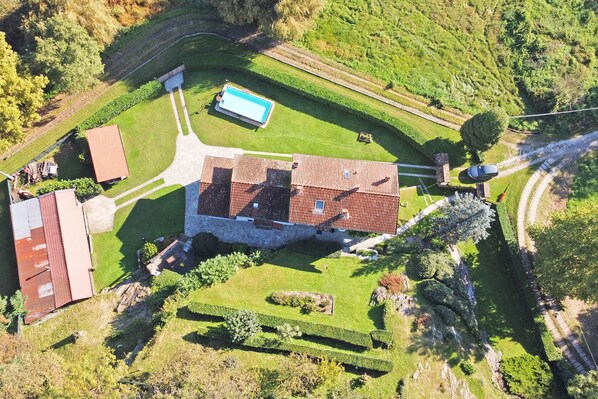 An aerial view of a property with a swimming pool, a red-roofed building, and a well-maintained lawn.