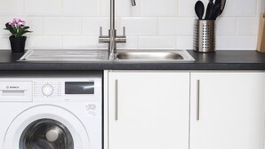 Une cuisine moderne dotée d’un lave-linge encastré, d’un évier en acier inoxydable et de meubles de rangement blancs.