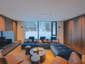A modern living room with a sectional sofa, a flat-screen TV, and a large window with a view of a snowy landscape.