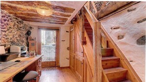 A rustic wooden interior with a desk, chair, and a staircase leading to a loft area.