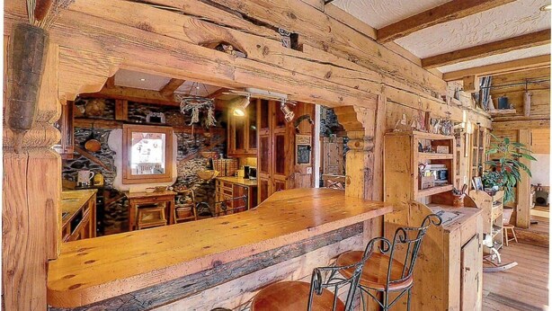 A rustic wooden interior with a bar area, stone walls, and metal chairs.