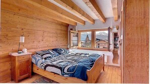 A wooden bedroom with a bed, a nightstand, and a window with a view of mountains.