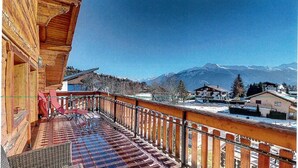 A wooden balcony with a view of snow-covered mountains and a clear sky.