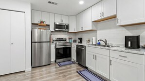 Una cocina moderna con electrodomésticos de acero inoxidable, armarios blancos y piso de madera.