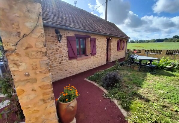Un bâtiment en pierre avec un chemin rouge menant à une table et à des chaises à l’extérieur.
