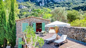 Una villa in pietra con terrazza in legno, mobili da esterno e vista su un paesaggio montuoso.