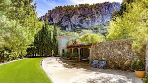Un edificio in pietra con patio, immerso nel verde e con le montagne sullo sfondo.