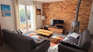 Un salon moderne avec une cheminée, des canapés, un téléviseur et une vue sur l’extérieur grâce à une porte vitrée.