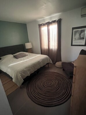 A hotel room with a bed, a round rug, a chair, a lamp, and a framed picture on the wall.
